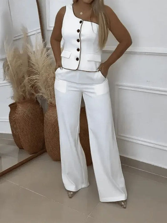 Conjunto de alfaiataria feminino branco com top cropped de um ombro só assimétrico e calça pantalona de cintura alta. Modelo posa de corpo inteiro mostrando o caimento elegante do look social.
